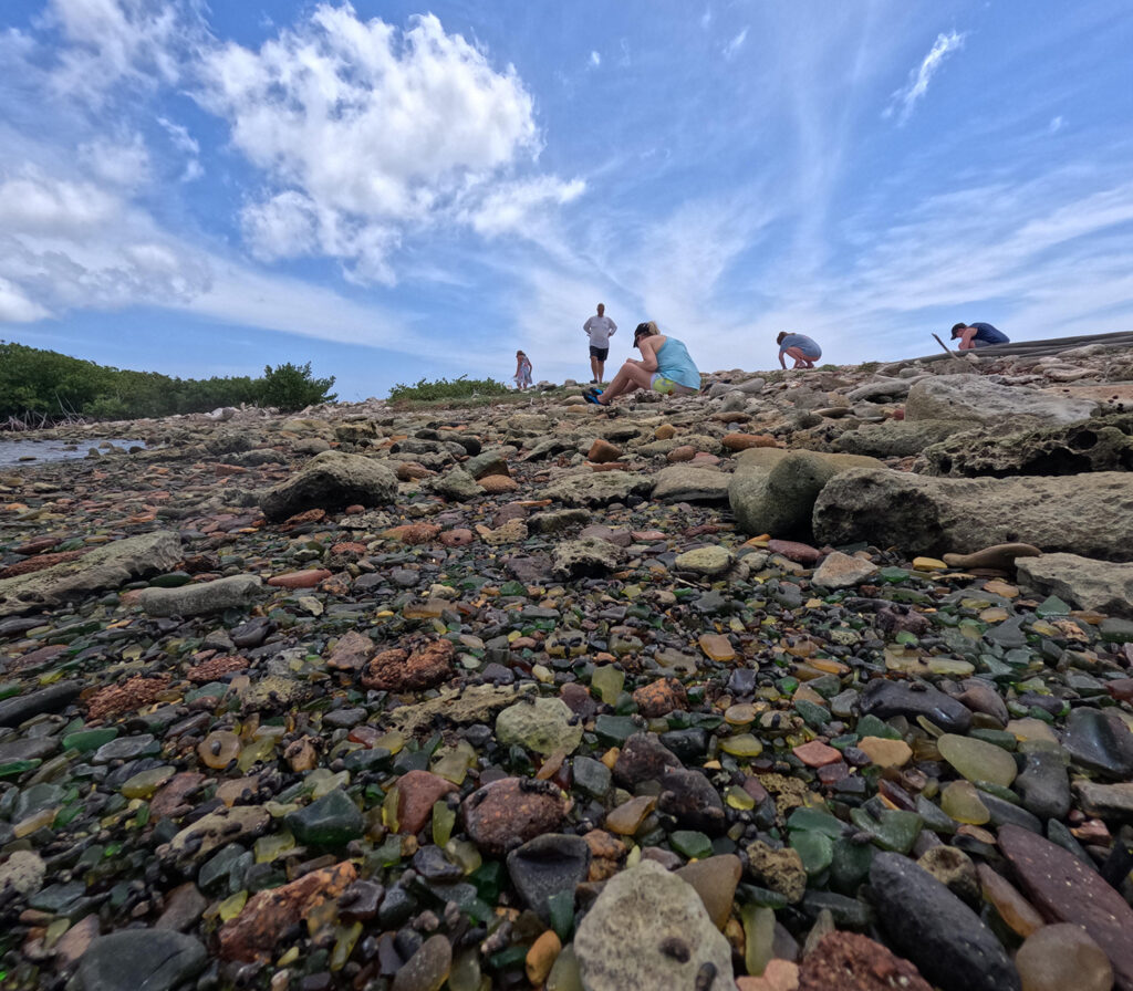 Tour participants search for sea glass along the rocky shore of Sea Glass Island Aruba.