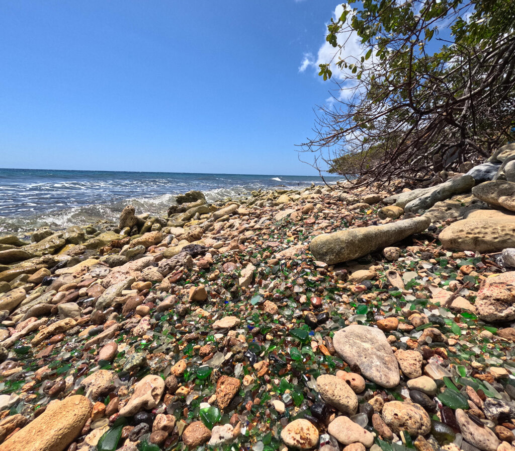 A stunning shoreline covered in sea glass and stones on Sea Glass Island Aruba, with ocean waves in the background.